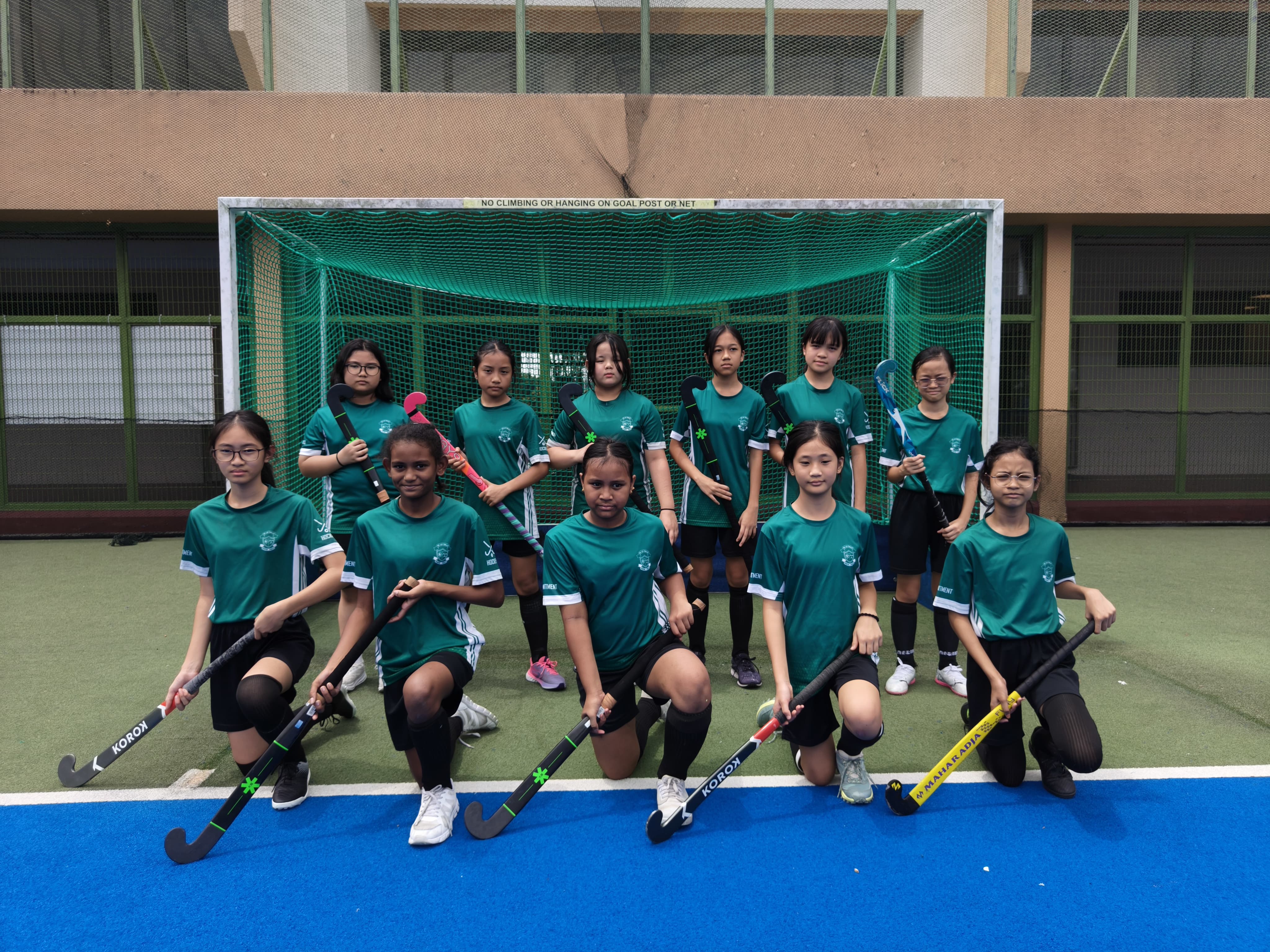 De La Salle School's girls hockey team posing with their hockey sticks in front of the goal net for a team photo.